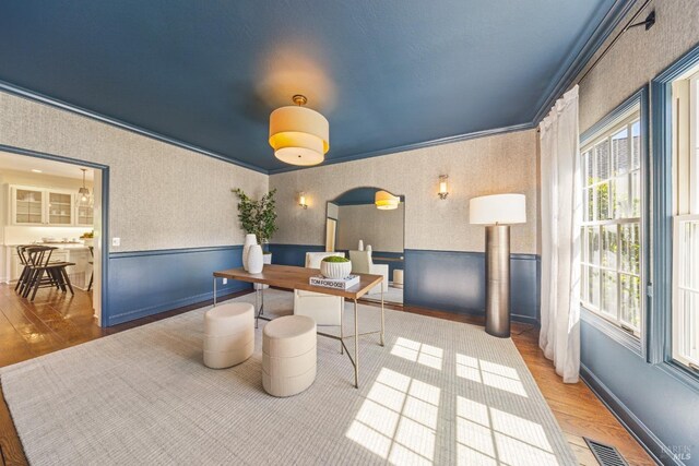 office space featuring visible vents, wallpapered walls, wood finished floors, and ornamental molding