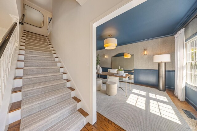 stairway with baseboards, wallpapered walls, wood finished floors, and visible vents