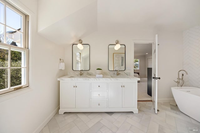full bath featuring double vanity, baseboards, a sink, and a freestanding bath