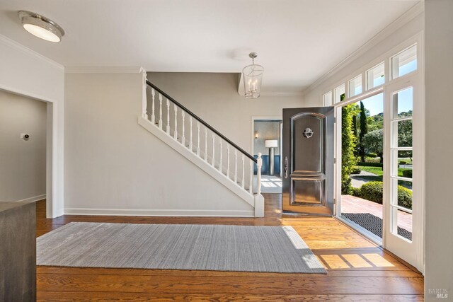 entryway with wood finished floors, crown molding, baseboards, and stairway