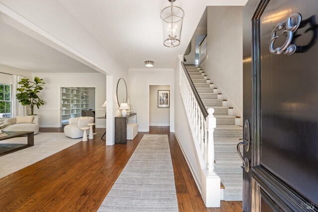 entrance foyer with stairway, ornamental molding, dark wood-type flooring, baseboards, and a notable chandelier