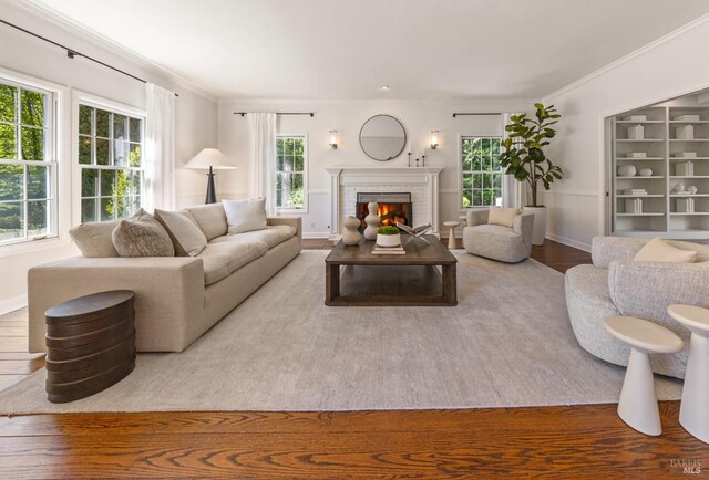 living area with wood finished floors, a brick fireplace, baseboards, and ornamental molding