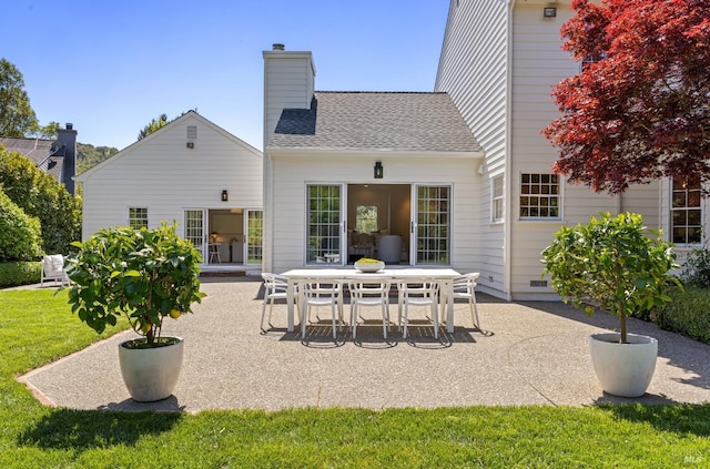 back of house featuring a chimney, a yard, a patio area, and a shingled roof