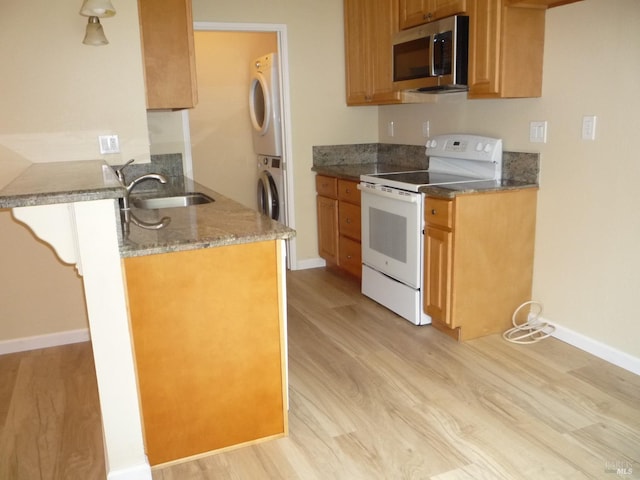 kitchen with baseboards, stacked washing maching and dryer, light wood-type flooring, stainless steel microwave, and electric stove