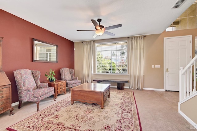 living area with a ceiling fan, baseboards, stairs, and light colored carpet