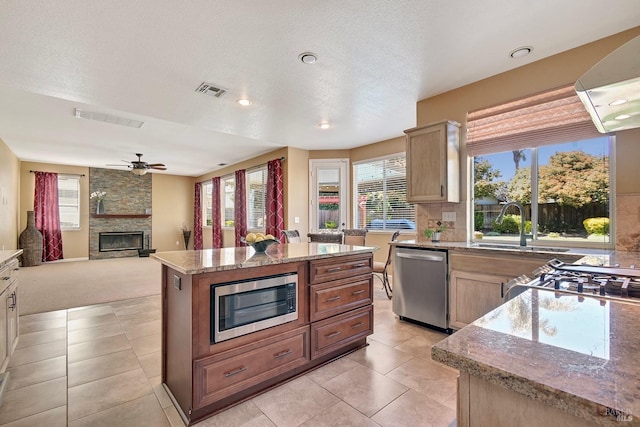 kitchen featuring a stone fireplace, ceiling fan, appliances with stainless steel finishes, light stone countertops, and visible vents