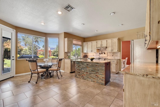 kitchen featuring a center island, decorative backsplash, baseboards, light stone countertops, and visible vents
