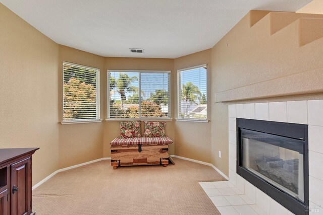 living area featuring visible vents, light carpet, a tile fireplace, and baseboards