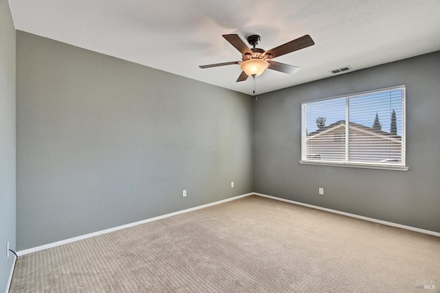 carpeted empty room featuring visible vents, a ceiling fan, and baseboards
