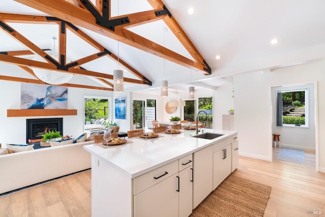 kitchen featuring a sink, an island with sink, open floor plan, light wood-type flooring, and white cabinetry