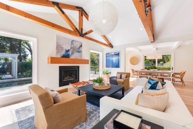 living area with a glass covered fireplace, a wealth of natural light, wood finished floors, and vaulted ceiling with beams