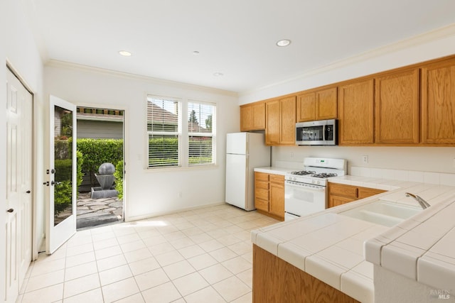 kitchen with a sink, white appliances, brown cabinetry, tile counters, and ornamental molding