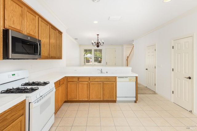 kitchen with an inviting chandelier, ornamental molding, a sink, white appliances, and a peninsula
