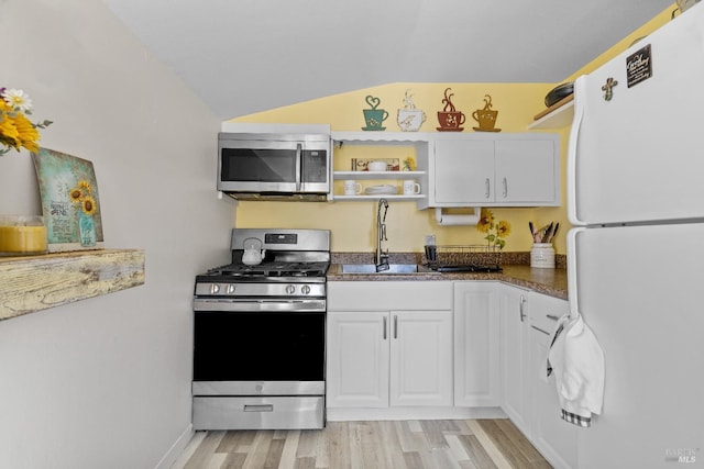 kitchen featuring a sink, light wood-style floors, stainless steel appliances, white cabinets, and lofted ceiling