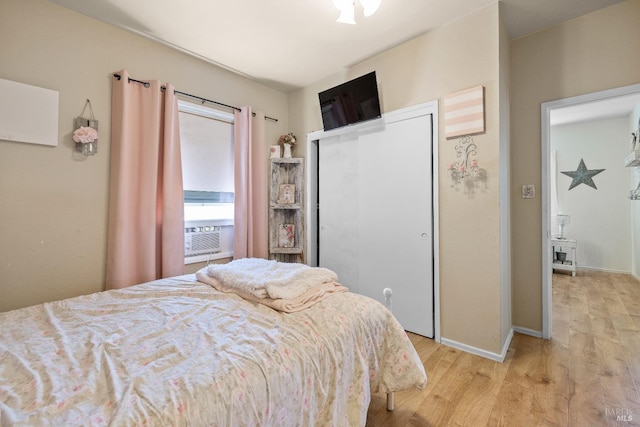 bedroom featuring cooling unit, light wood-style flooring, baseboards, and a closet