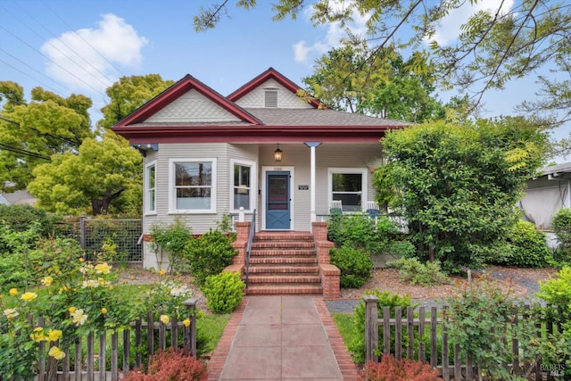 bungalow-style house featuring a porch, a shingled roof, and fence