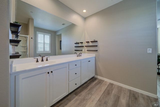 bathroom featuring a sink, double vanity, baseboards, a shower stall, and wood finished floors