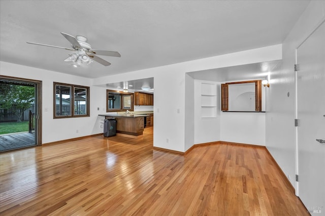 unfurnished living room with light wood finished floors, baseboards, and a ceiling fan