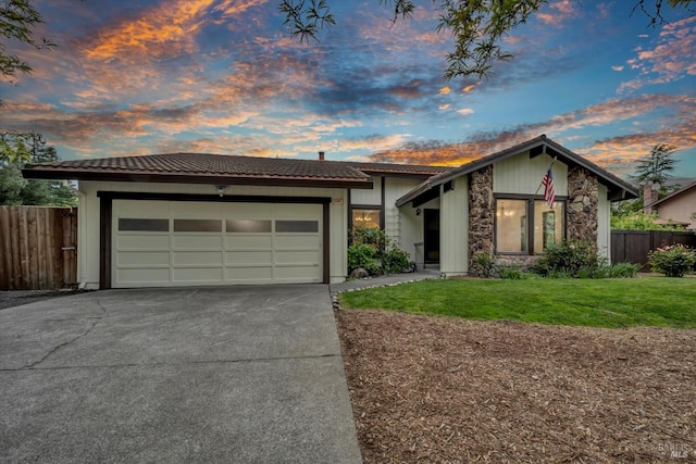 view of front of house with concrete driveway, an attached garage, fence, and a lawn