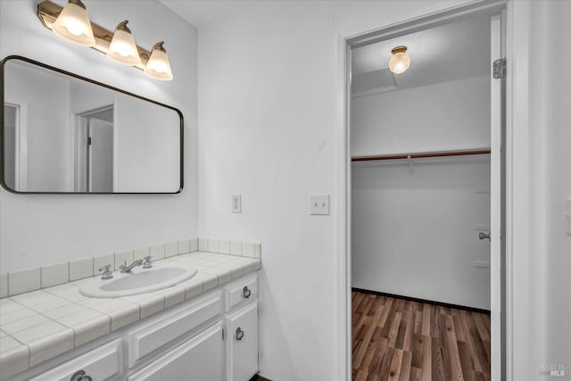 bathroom with a walk in closet, wood finished floors, and vanity