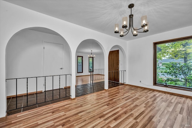 unfurnished room with a chandelier, plenty of natural light, and wood finished floors