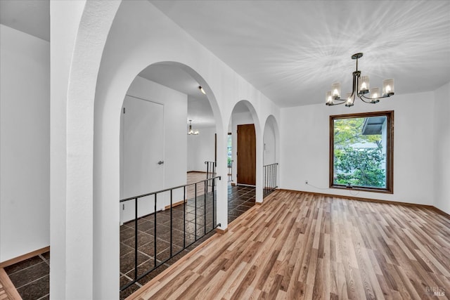 unfurnished room with arched walkways, a chandelier, and wood finished floors