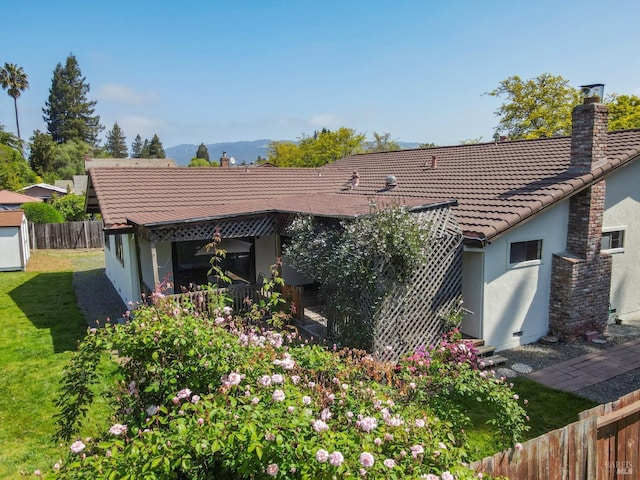 back of house with a chimney, a yard, fence, stucco siding, and a tile roof