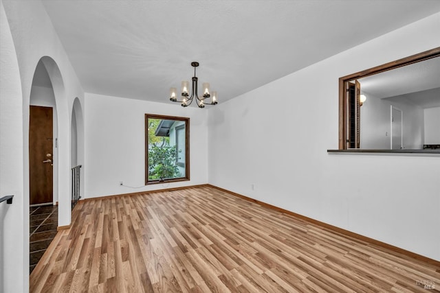 empty room with light wood finished floors, arched walkways, baseboards, and a notable chandelier