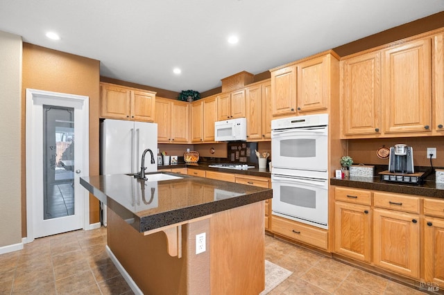 kitchen with light brown cabinets, white appliances, a kitchen breakfast bar, a center island with sink, and a sink