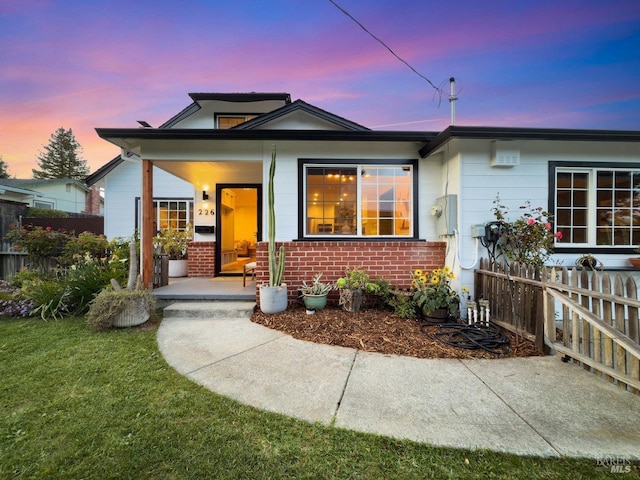 view of front of property featuring brick siding, fence, a porch, and a lawn
