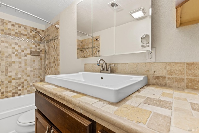 full bathroom with vanity, toilet, stone tile floors, shower / bath combination, and visible vents