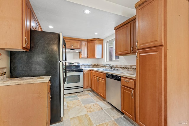 kitchen with stone finish flooring, a sink, light countertops, under cabinet range hood, and stainless steel appliances