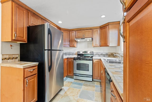 kitchen featuring stone finish flooring, a sink, under cabinet range hood, stainless steel appliances, and recessed lighting