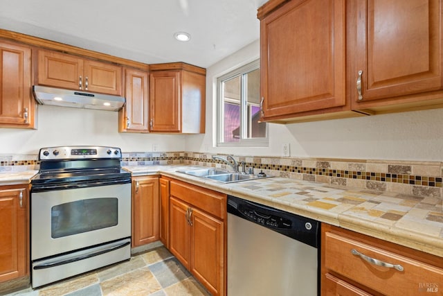 kitchen with brown cabinetry, a sink, appliances with stainless steel finishes, and under cabinet range hood