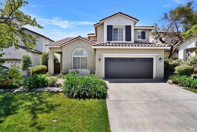 mediterranean / spanish house featuring stucco siding, a tile roof, a garage, and concrete driveway