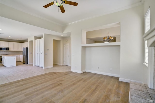 unfurnished living room featuring ceiling fan with notable chandelier, baseboards, a wealth of natural light, and crown molding