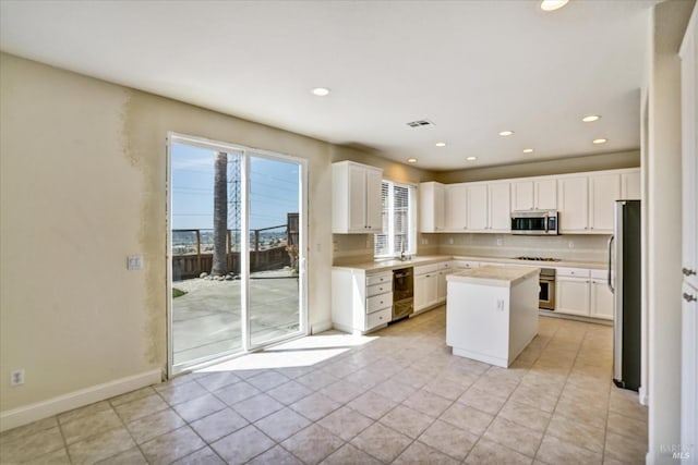 kitchen with white cabinets, appliances with stainless steel finishes, light countertops, a kitchen island, and light tile patterned floors