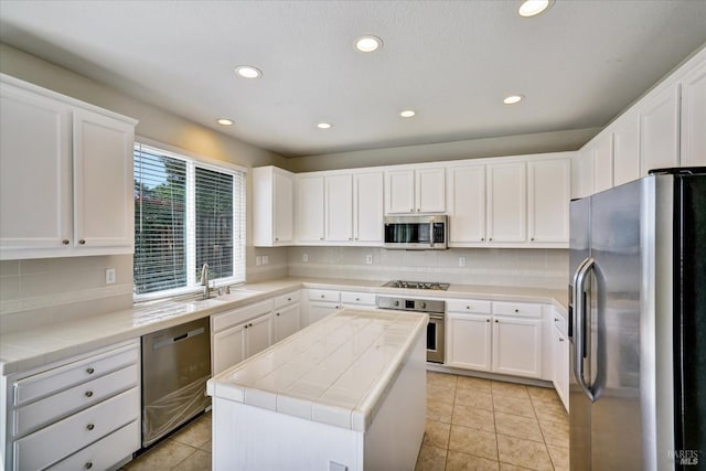 kitchen with recessed lighting, tile countertops, a sink, a kitchen island, and appliances with stainless steel finishes