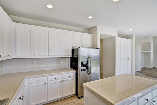 kitchen with tile countertops, decorative backsplash, and stainless steel refrigerator with ice dispenser