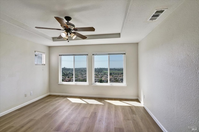 unfurnished room featuring a tray ceiling, wood finished floors, baseboards, and a textured wall