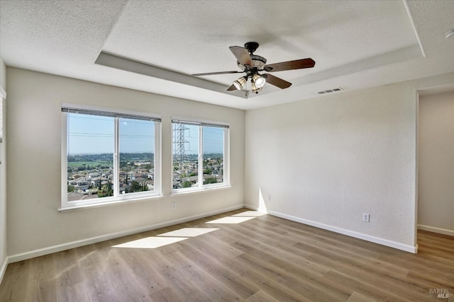 empty room with a tray ceiling, baseboards, visible vents, a ceiling fan, and wood finished floors
