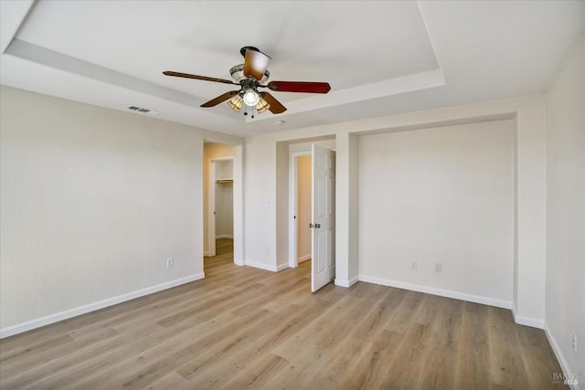 unfurnished bedroom featuring baseboards, wood finished floors, visible vents, and a raised ceiling