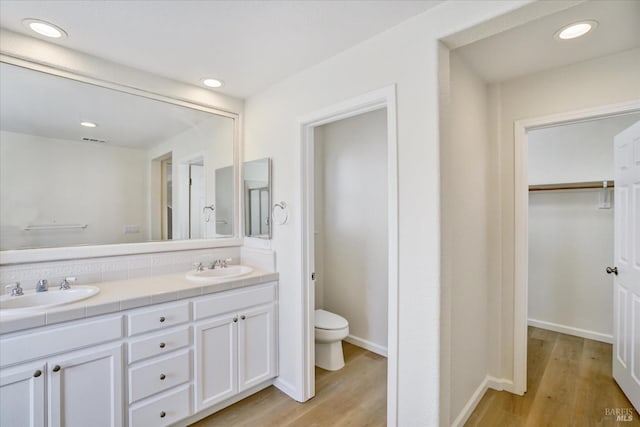 bathroom with double vanity, wood finished floors, visible vents, toilet, and a sink
