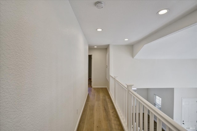 hall with an upstairs landing, baseboards, wood finished floors, and recessed lighting