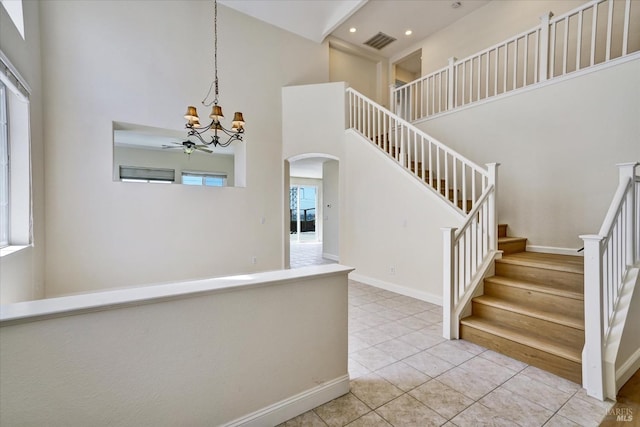 staircase featuring arched walkways, visible vents, a towering ceiling, ceiling fan with notable chandelier, and tile patterned flooring