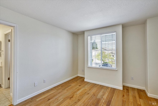 spare room featuring light wood-type flooring, a textured ceiling, and baseboards