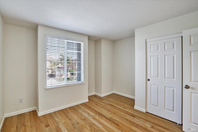 unfurnished bedroom featuring light wood-type flooring, a textured ceiling, and baseboards