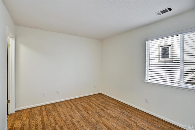 unfurnished room with wood finished floors, visible vents, and baseboards