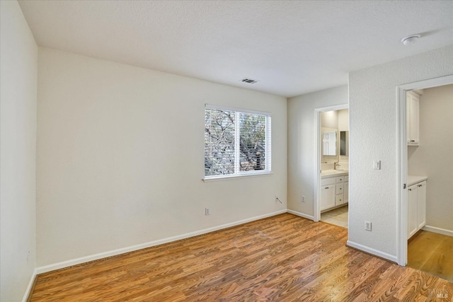 unfurnished bedroom featuring a spacious closet, visible vents, connected bathroom, light wood-type flooring, and baseboards