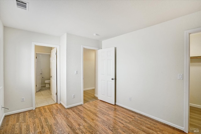 unfurnished bedroom with baseboards, wood finished floors, visible vents, and ensuite bathroom